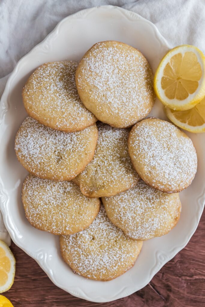 lemon cookies on white platter sprinkled with powdered sugar