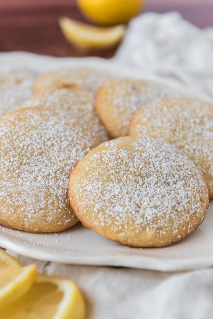 closeup view of lemon cookies covered with powdered sugar and lemon slices in background