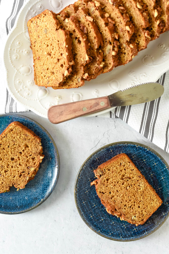 overhead view of two slices of pumpkin bread on blue plates next to more slices on white platter