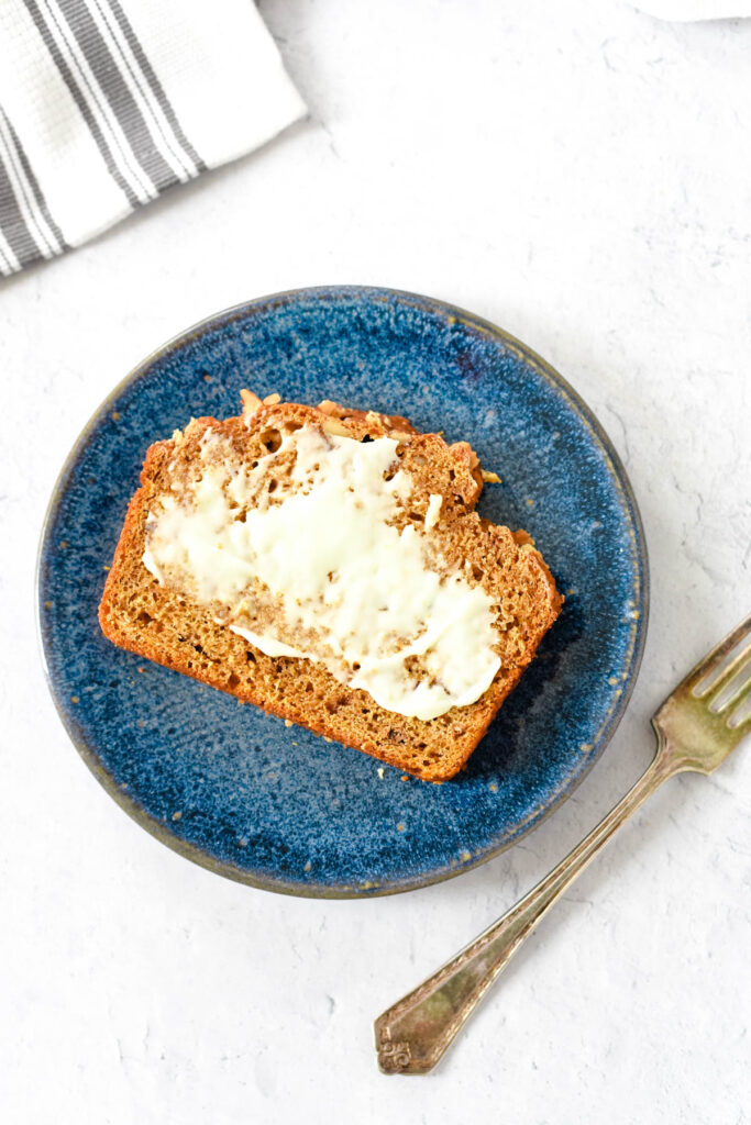 overhead view of one slice of sourdough pumpkin bread on blue plate smeared with butter, with fork off to the side