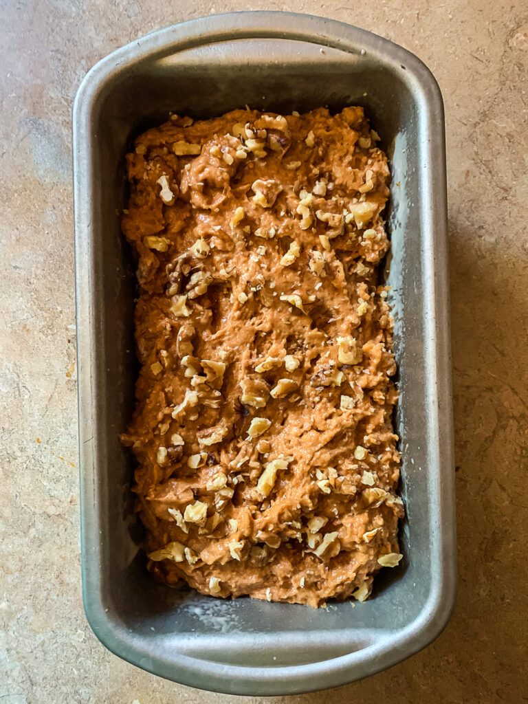 pumpkin bread batter in metal baking tin with crushed walnuts on top