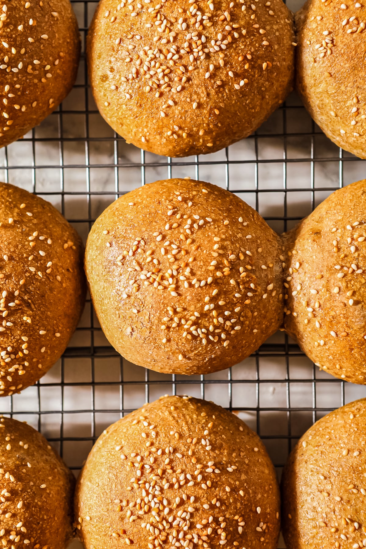 sourdough hamburger buns with sesame seeds on wire cooling rack