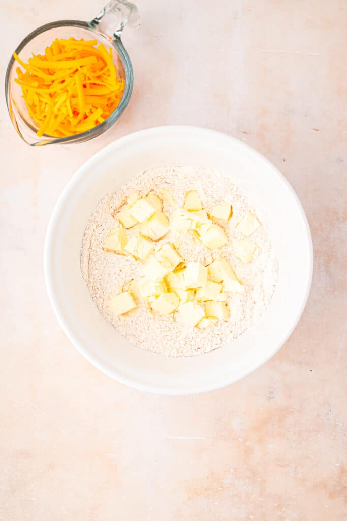 white mixing bow with dried ingredients and cubes of butter to mix in