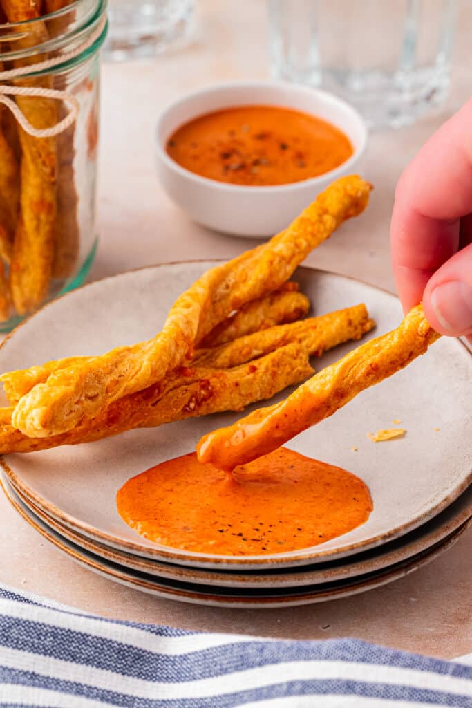 hand dipping cheese straw into dip on white plate