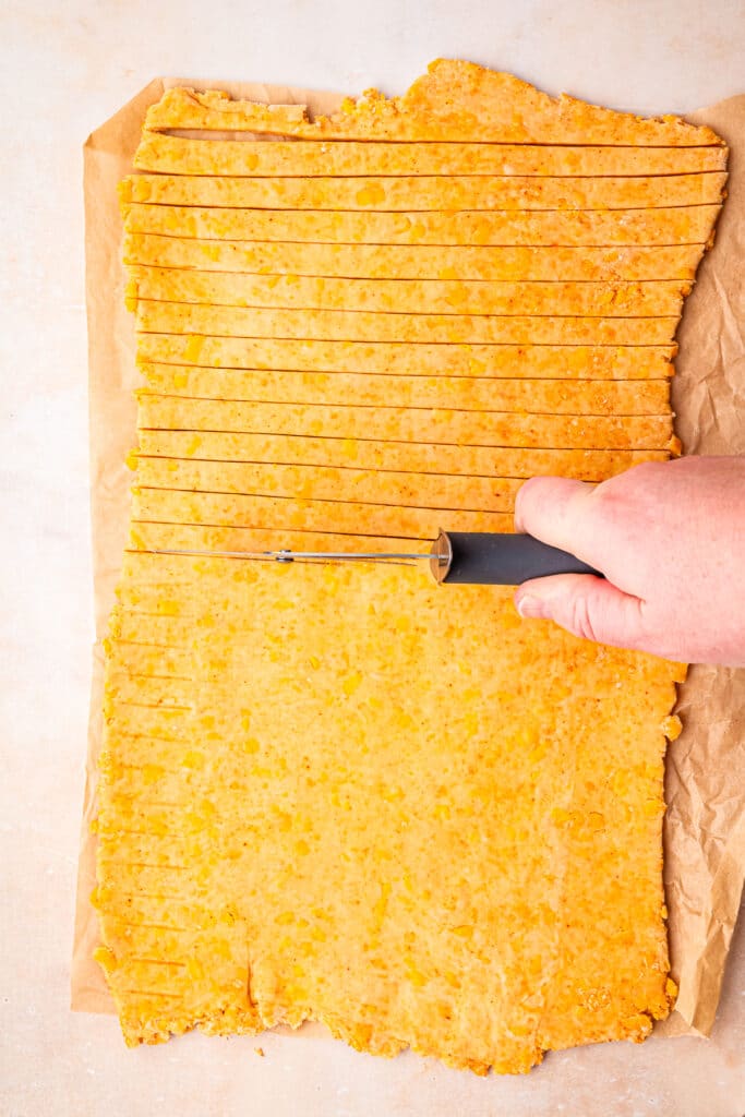 hand using pizza cutter to slice dough into thin strips
