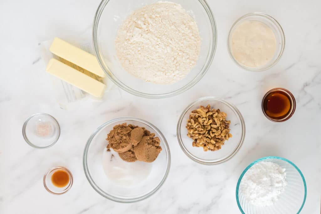 ingredients for sourdough maple walnut cookies in glass bowls on marble counter