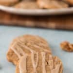 two maple walnut cookies wtih drizzle resting on each other with tray in background