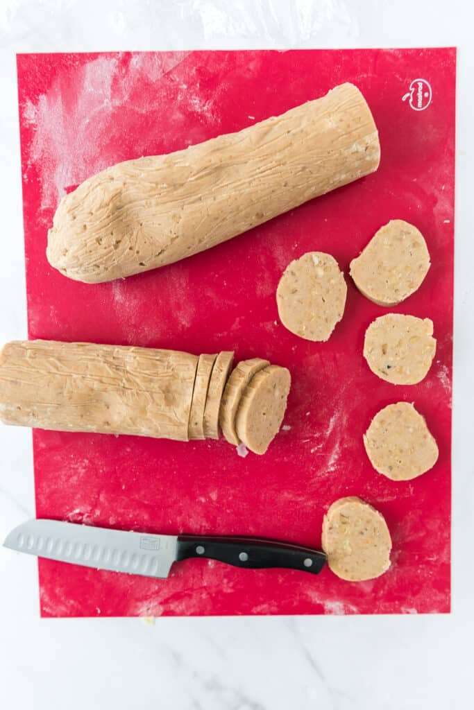 cookie dough logs being sliced on red silicone sheet