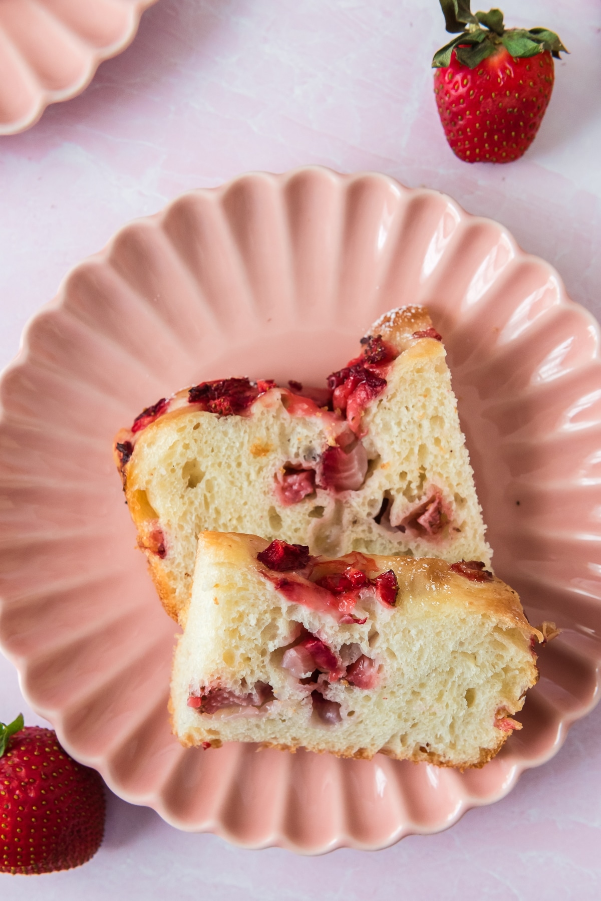 overhead view of pink plate with two slices of strawberry sourdough focaccia with strawberries around plate