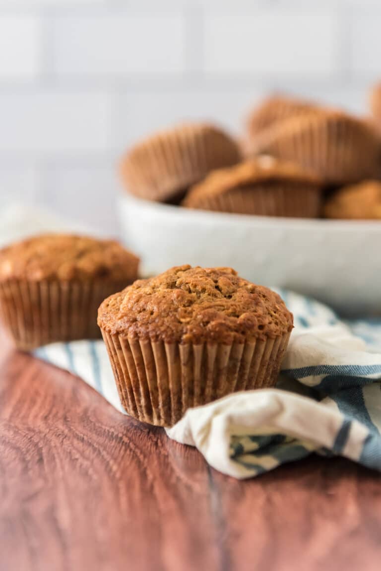 sourdough applesauce muffins on table with kitchen towel and bowl of more muffins in background