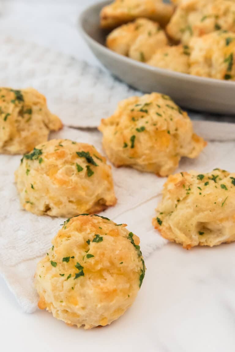 sourdough discard cheddar drop biscuits with parsley and garlic butter on white counter with grey bowl of more biscuits in background