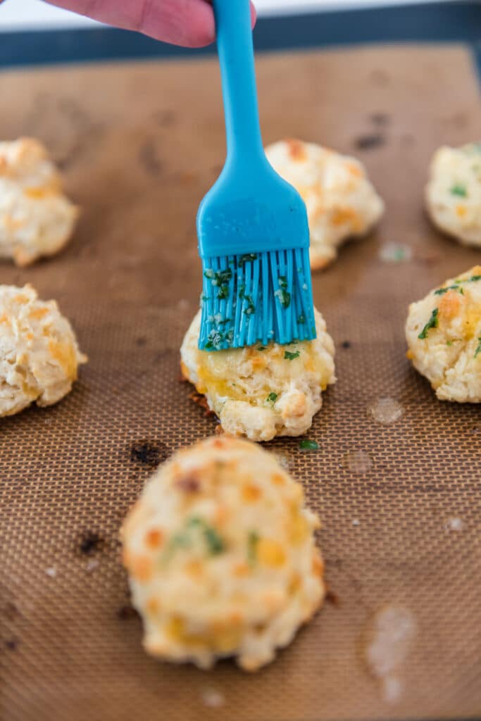 blue silicone pastry brush brushing melted butter on baked drop biscuits