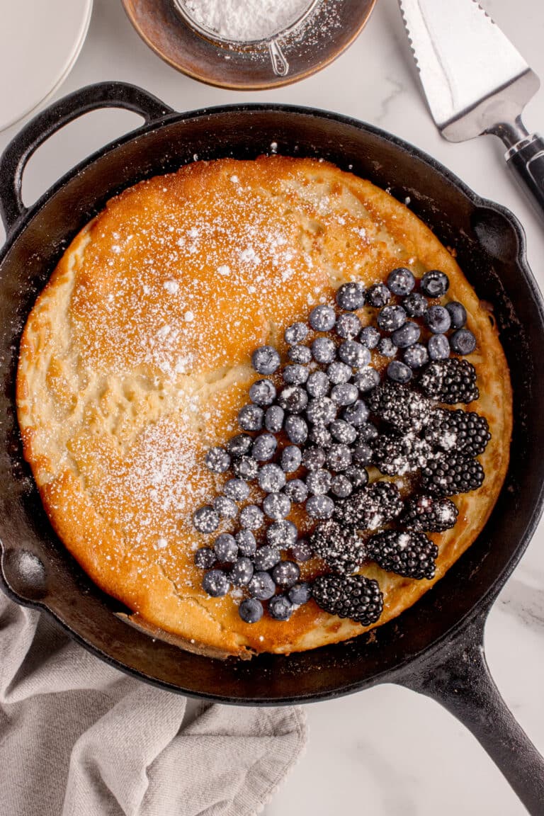 overhead view of cast iron skillet with sourdough dutch baby topped with blueberries, blackberries and powdered sugar