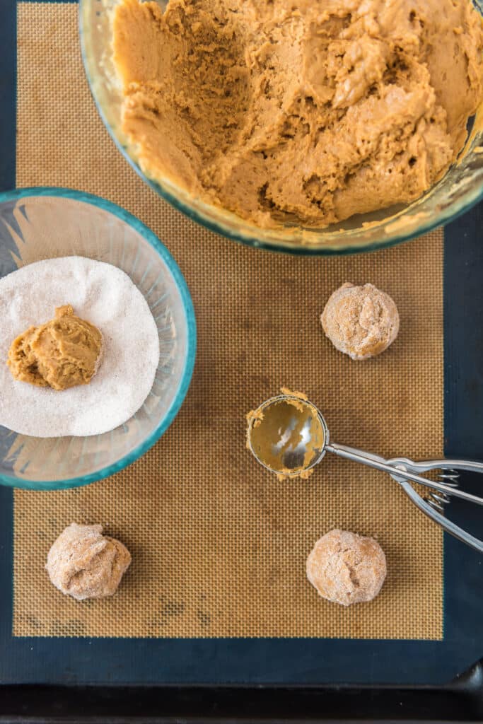 scooping cookie batter onto cookie sheet and rolling in cinnamon sugar