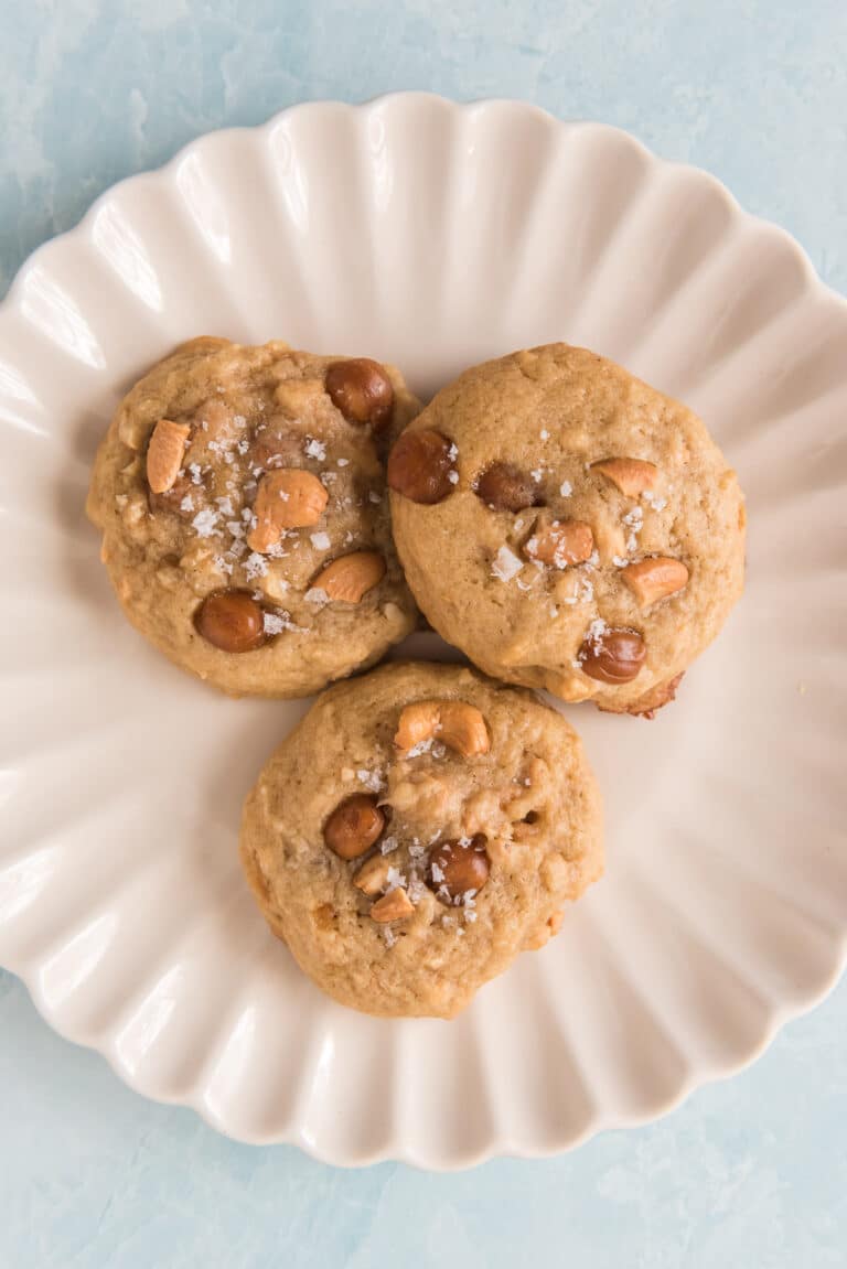 overhead of three sourdough cashew caramel cookies on white plate sprinkled with flaky sea salt