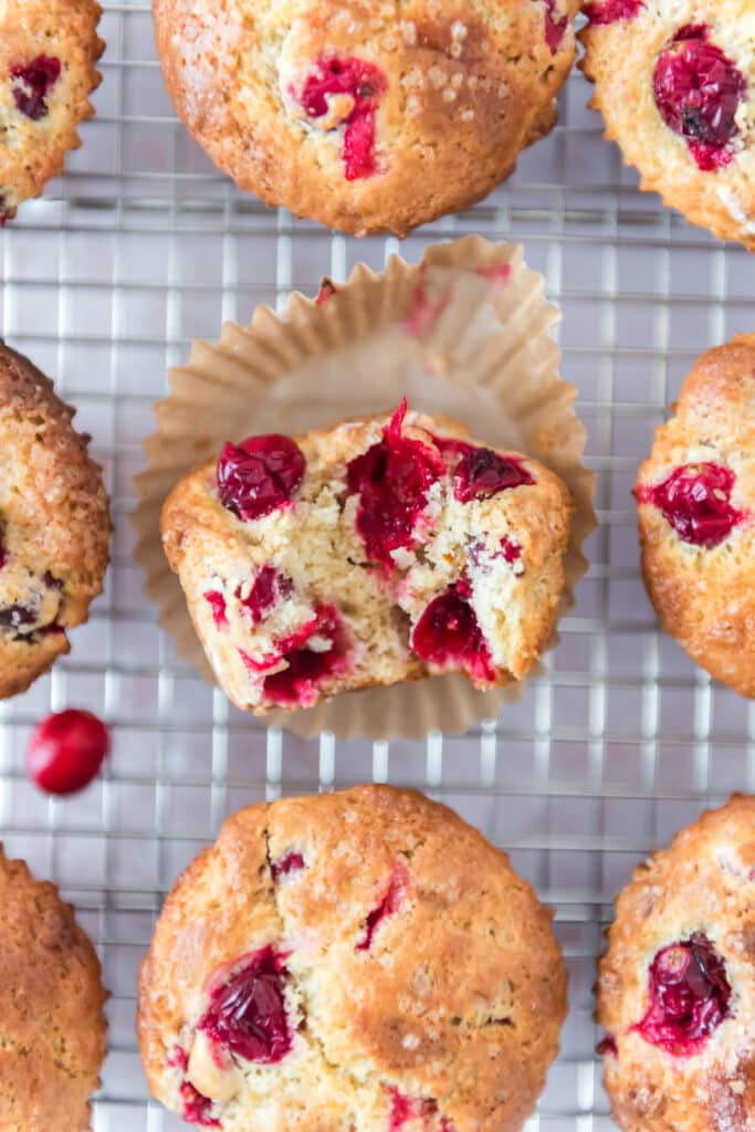 overhead view of cranberry muffins on wire rack with middle muffin out of the wrapper and a bite taken out