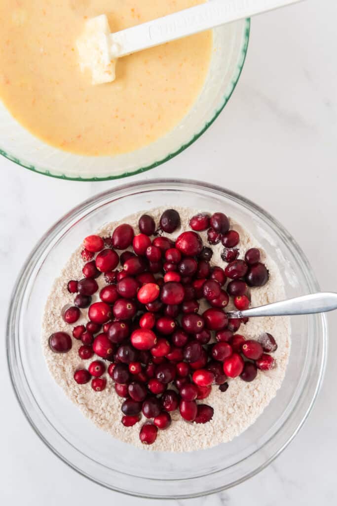 mixing bowl with dry ingredients for muffins with cranberries on top and bowl of batter in corner