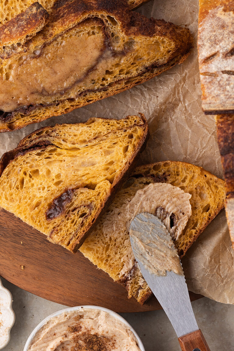slices of pumpkin cinnamon swirl sourodugh bread on cutting board beside loaf with knife spreading maple butter on