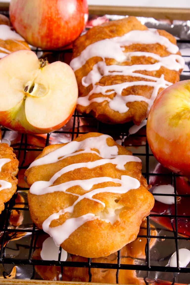 sourdough apple fritters on cooling rack with sliced apples around them
