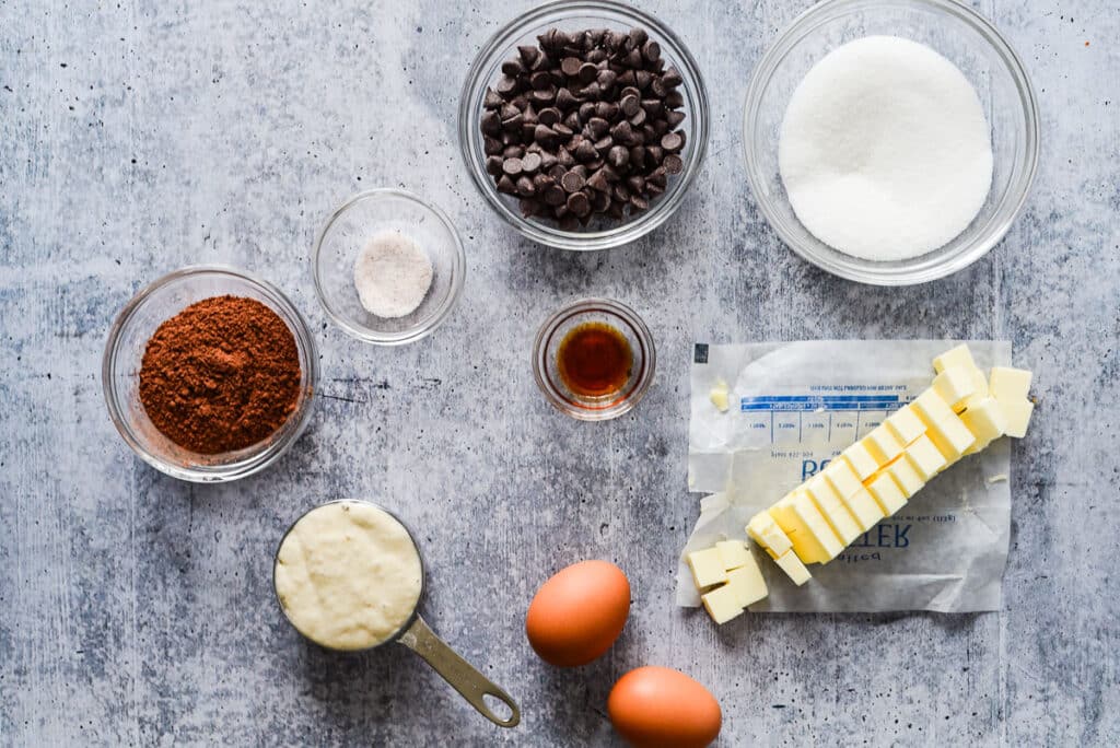 ingredients for sourdough brownies in glass bowls on blue counter
