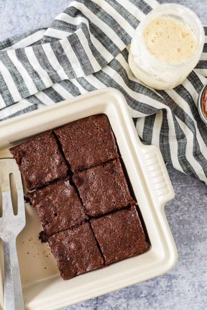 white pan with sourdough brownies next to jar of sourdough starter