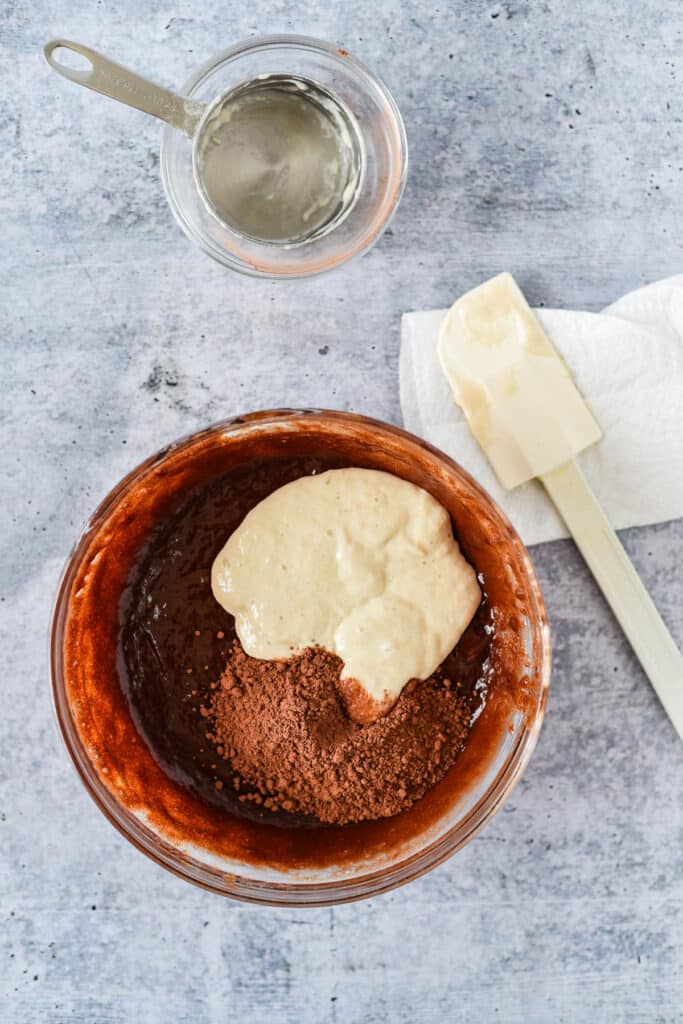 glass mixing bowl with ingredients for sourdough brownies and white rubber spatula beside bowl