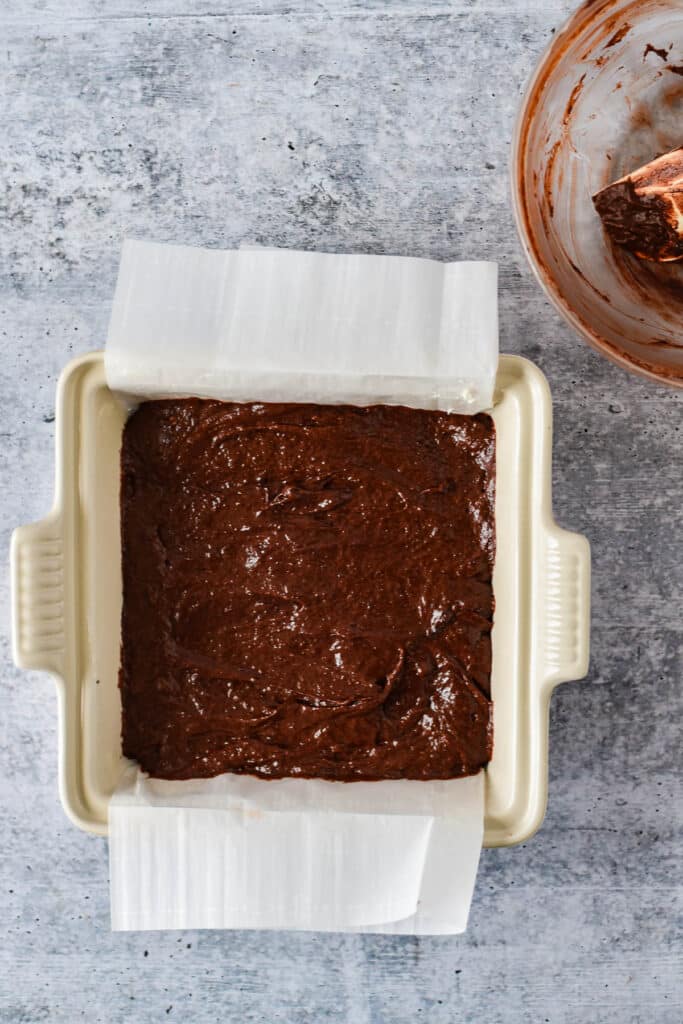 brownie batter poured into white 8x8 baking pan with parchment paper liner