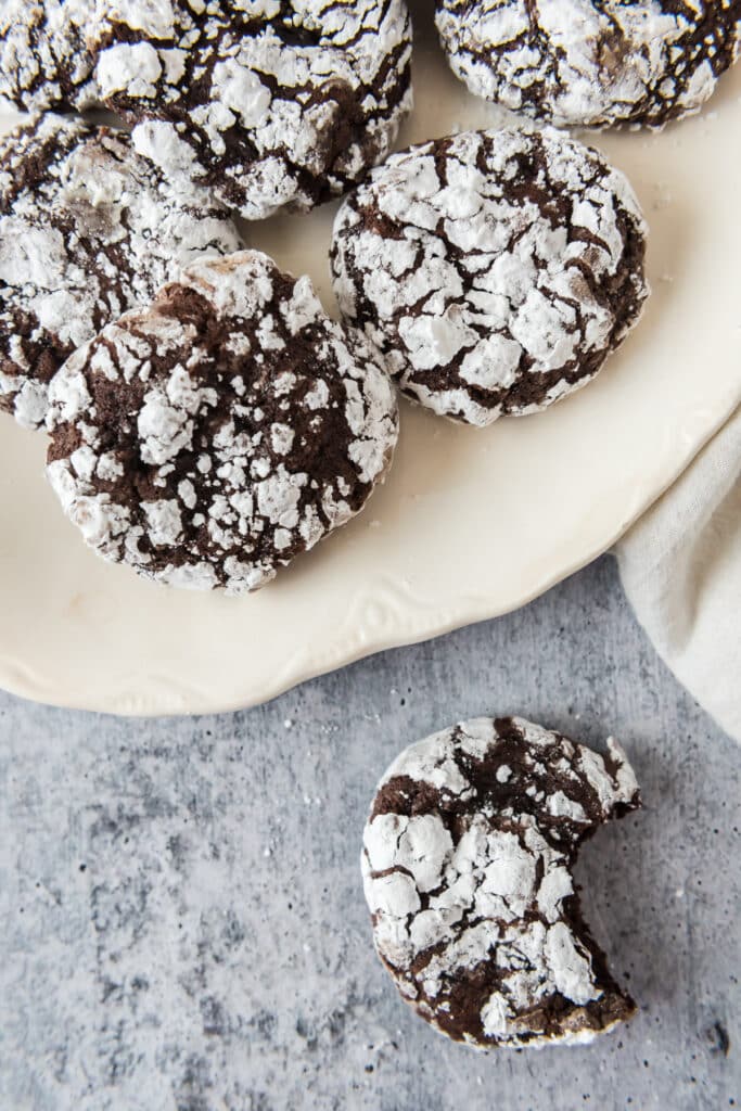 sourdough chocolate crinkle cookies on white platter with one cookie off to side with bite taken out