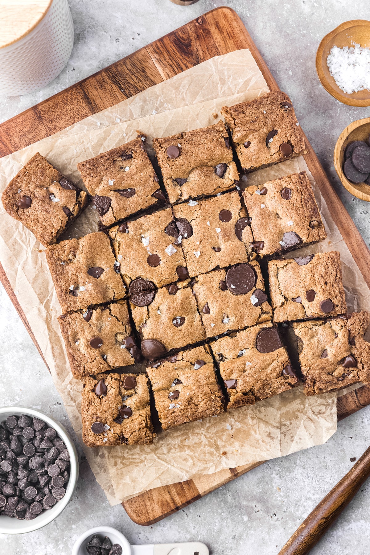 sourdough chocolate chip cookie bars cut on wooden cutting board with flakey sea salt and chocolate chips sprinkled around