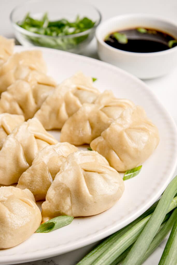 white plate with sourdough dumplings with beef filling and small bowl of soy sauce in background