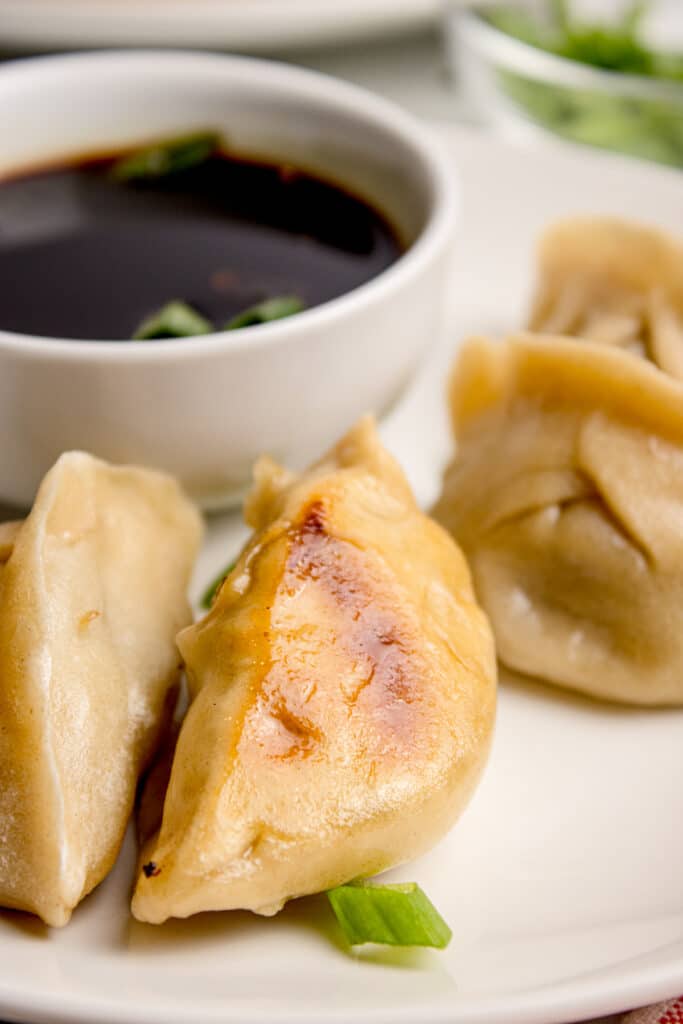 white plate with four dumplings with sourdough discard wrappers and beef filling with bowl of soy sauce in background