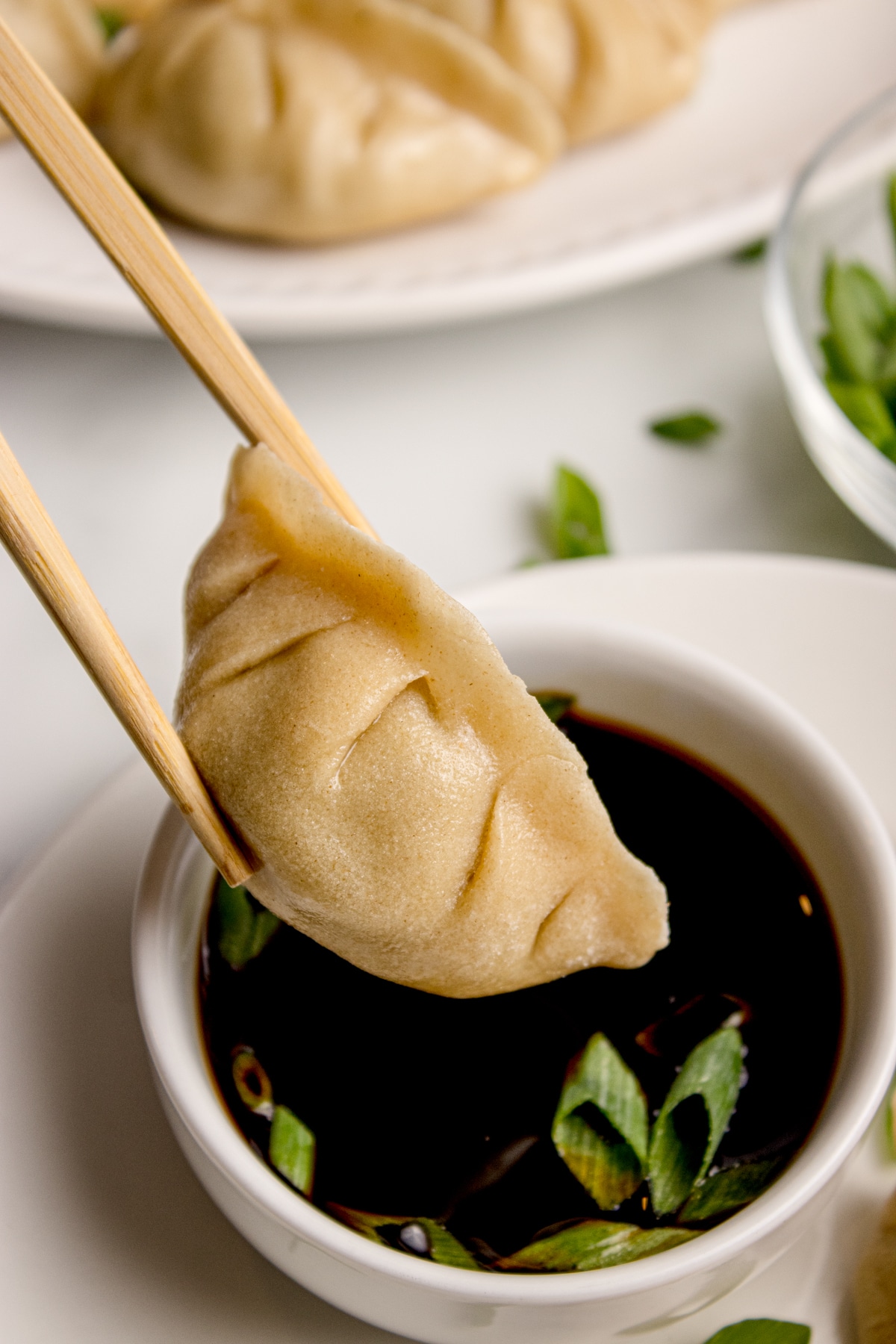 chopsticks holding beef dumpling with sourdough wrapper over small bowl of soy sauce
