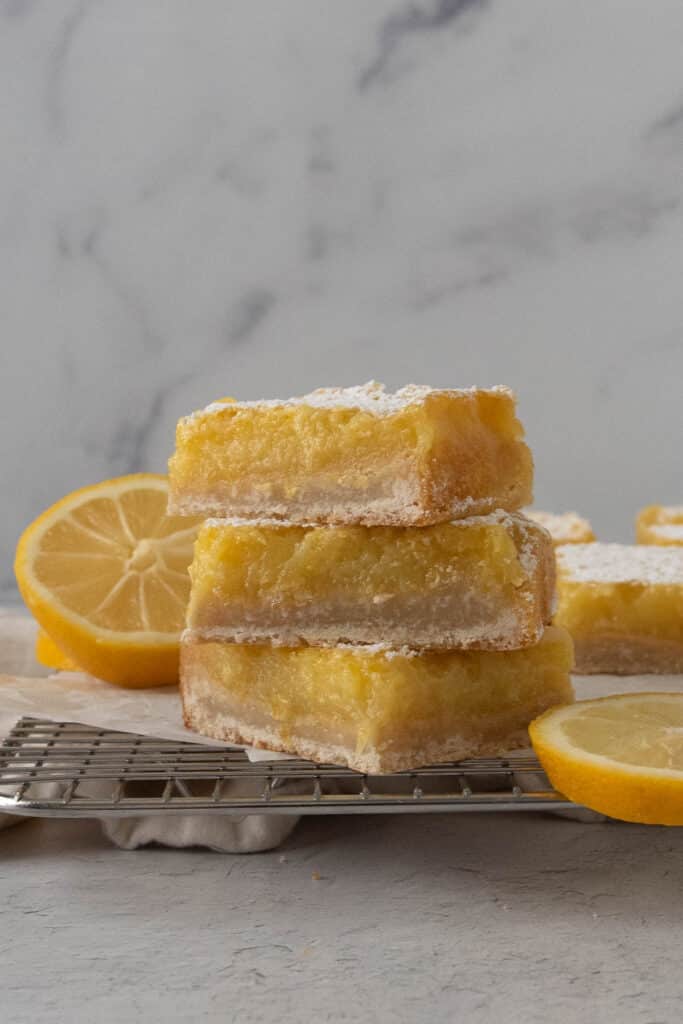 a stack of three sourdough lemon bars on a wire cooling rack with lemon slices around it