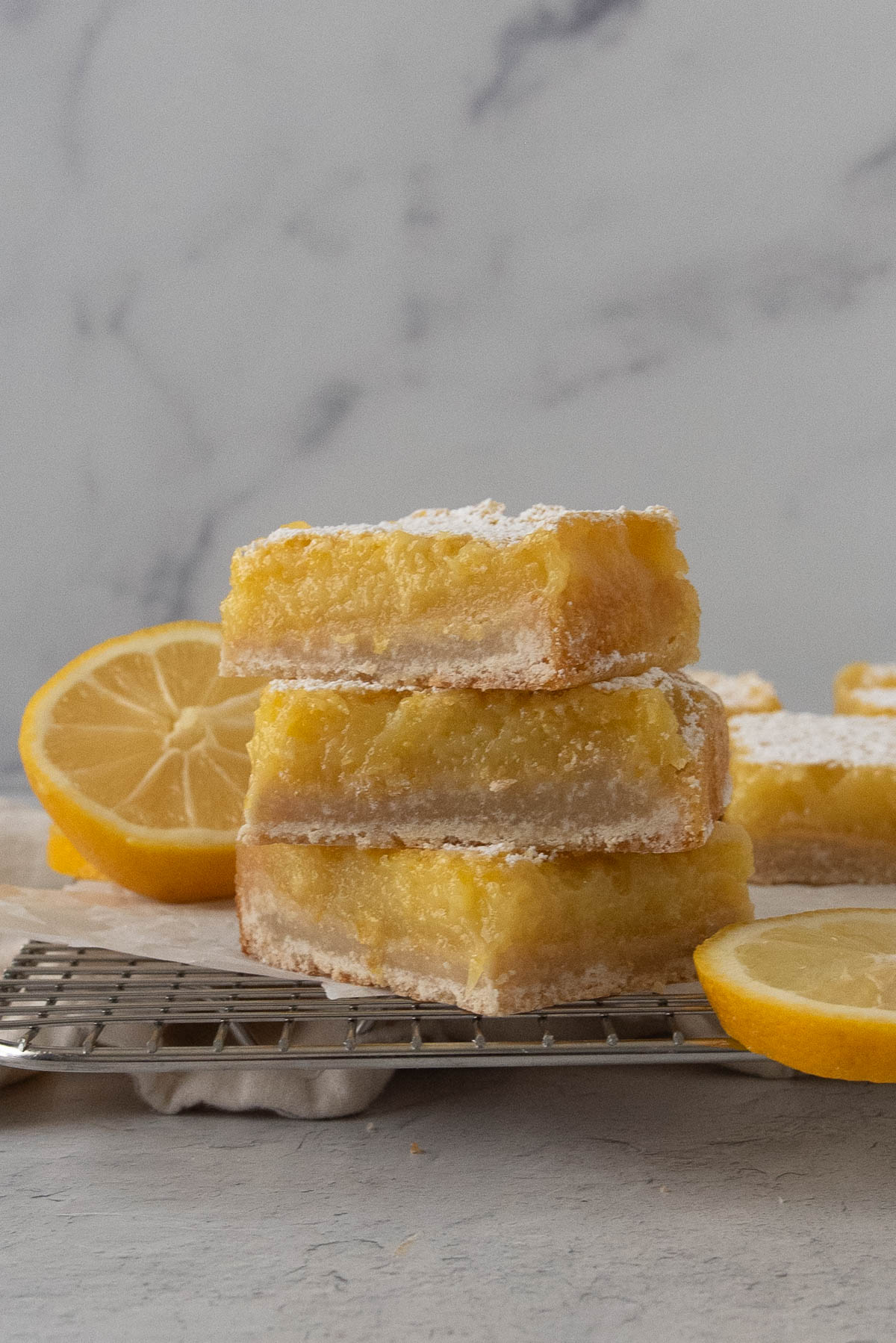 a stack of three sourdough lemon bars on a wire cooling rack with lemon slices around it