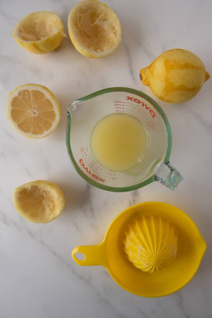 glass measuring cup with lemons and lemon juice being squeezed