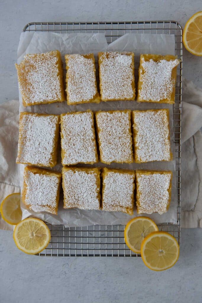 overhead view of sourdough lemon bars with powdered sugar arranged on metal cooling rack with lemon slices
