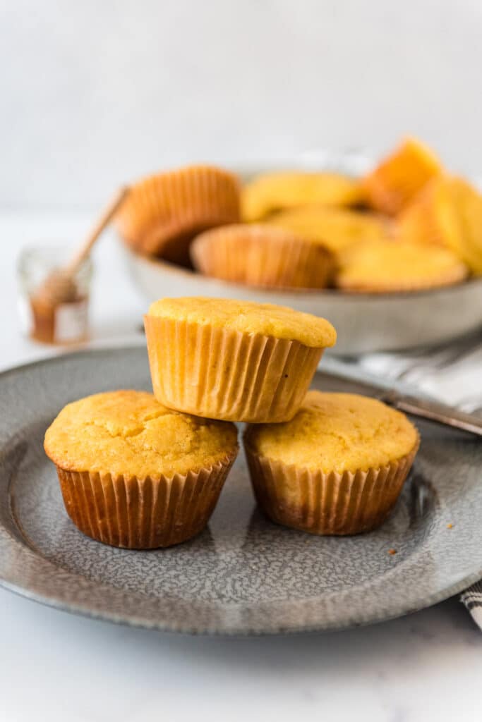 plate with three stacked sourdough corn muffins with bowl of more muffins in background