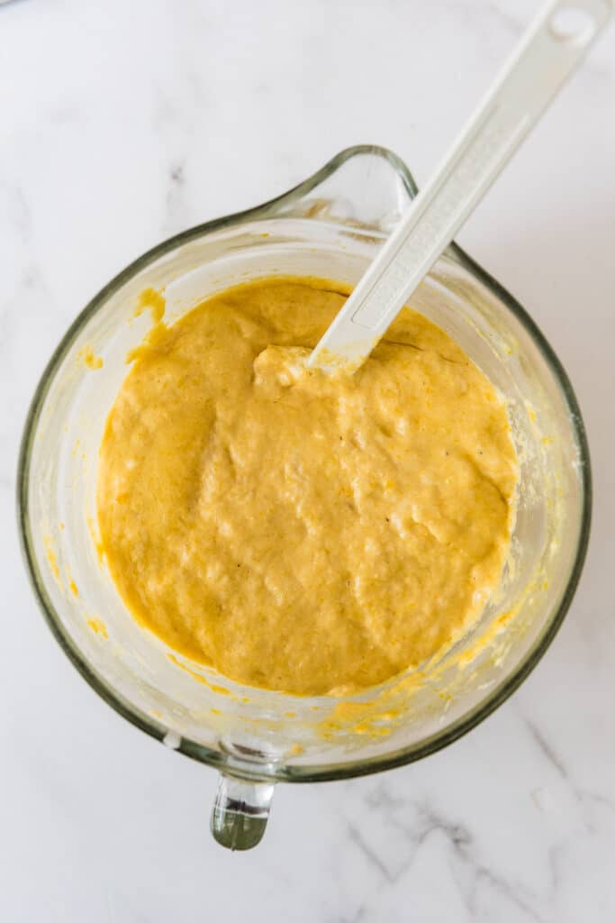 overhead view of glass mixing bowl with white spatula filled with cornbread batter with discard