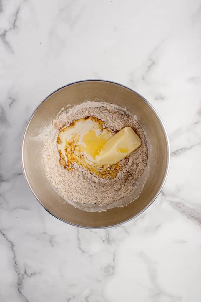 metal mixing bowl with mixed dry ingredients and sourdough starter and stick of butter