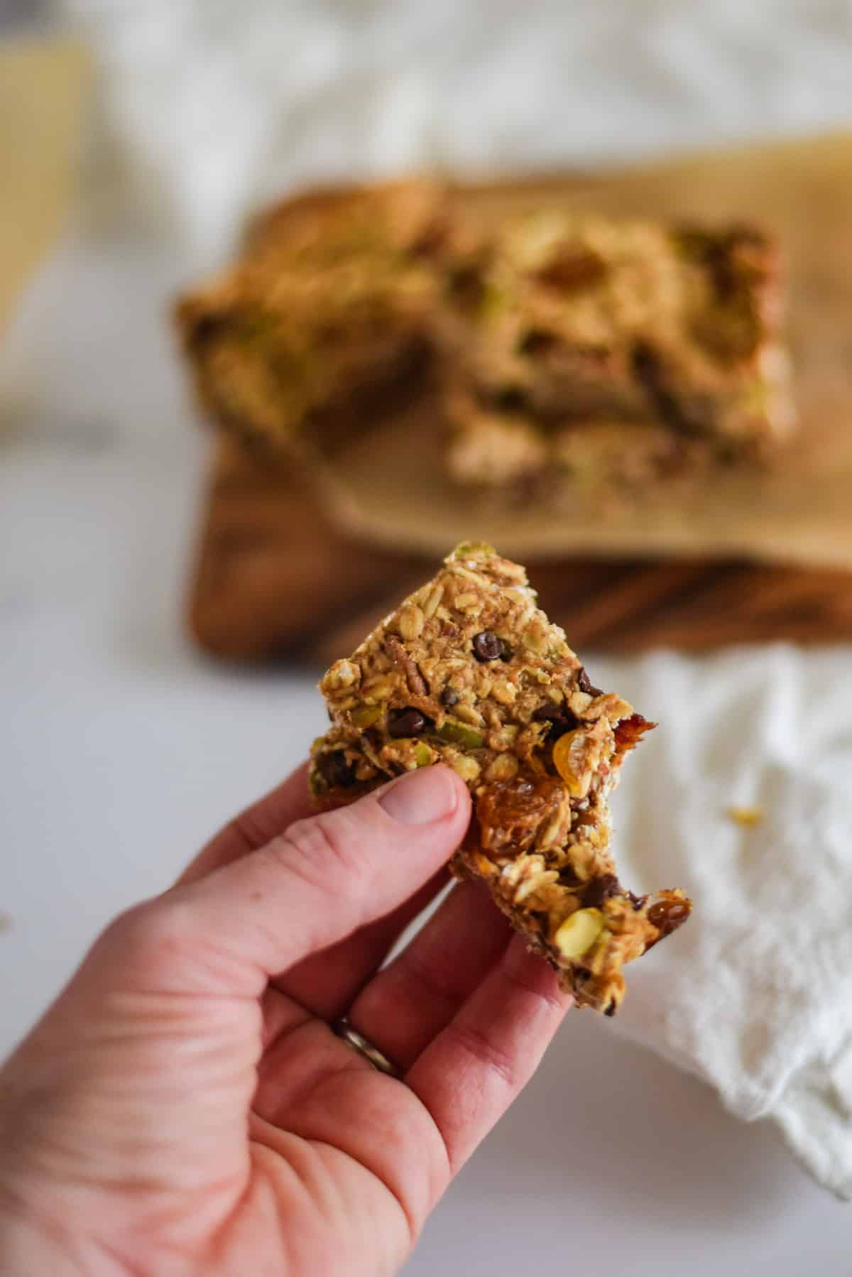 hand holding a sourdough granola bar over cutting board where more granola bars are stacked