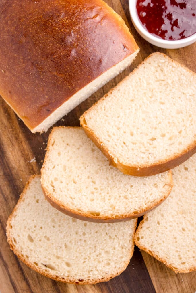 slices of potato flake bread stacked on board beside loaf
