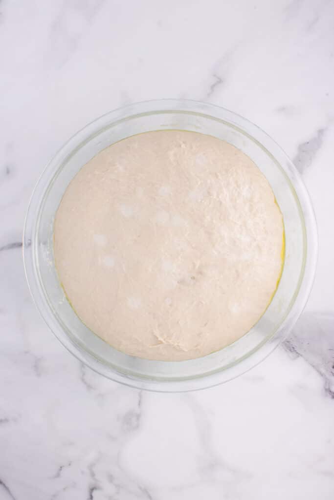 large glass mixing bowl with bread dough after doubling
