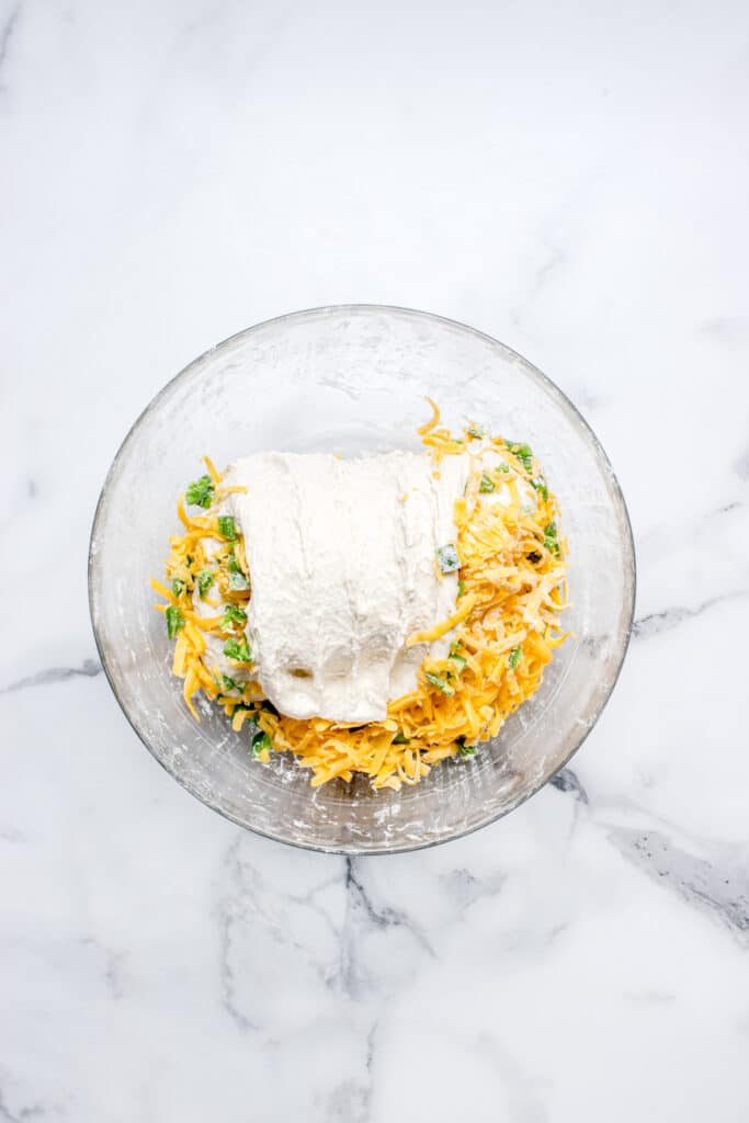 glass mixing bowl with bread dough and shredded cheese and jalapeno being mixed into dough