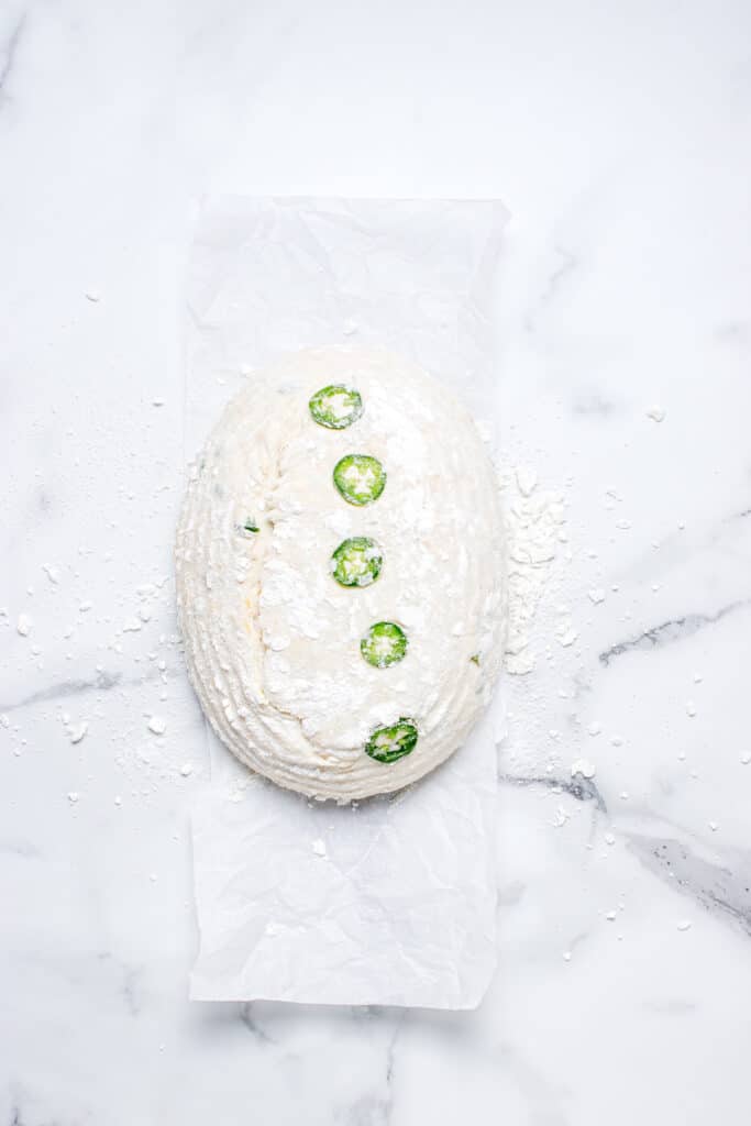 sourdough bread dough on parchment with jalapeno slices arranged in a line down the center and scored marks