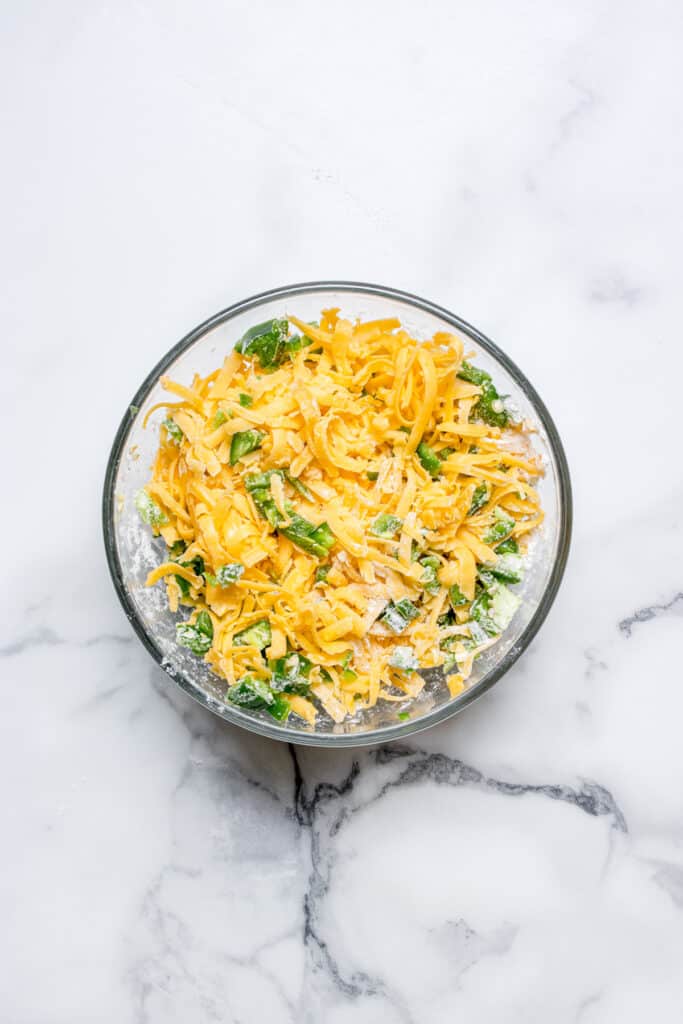 glass bowl with shredded cheddar cheese and minced jalapeno