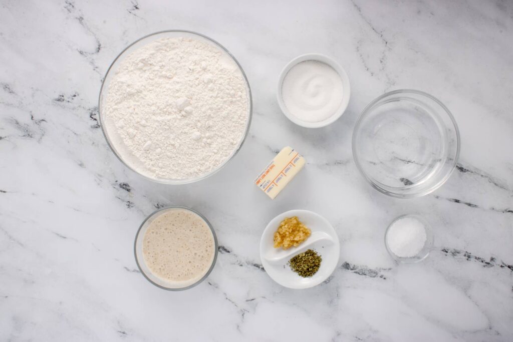 ingredients for sourdough breadsticks in glass bowls on marble counter