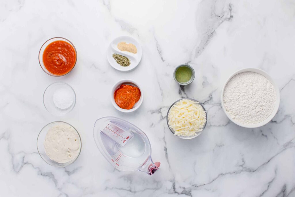ingredients for sourdough focaccia pizza in glass bowls on marble counter