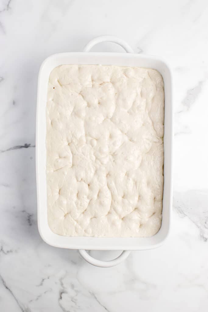 focaccia dough in white baking dish with dimples