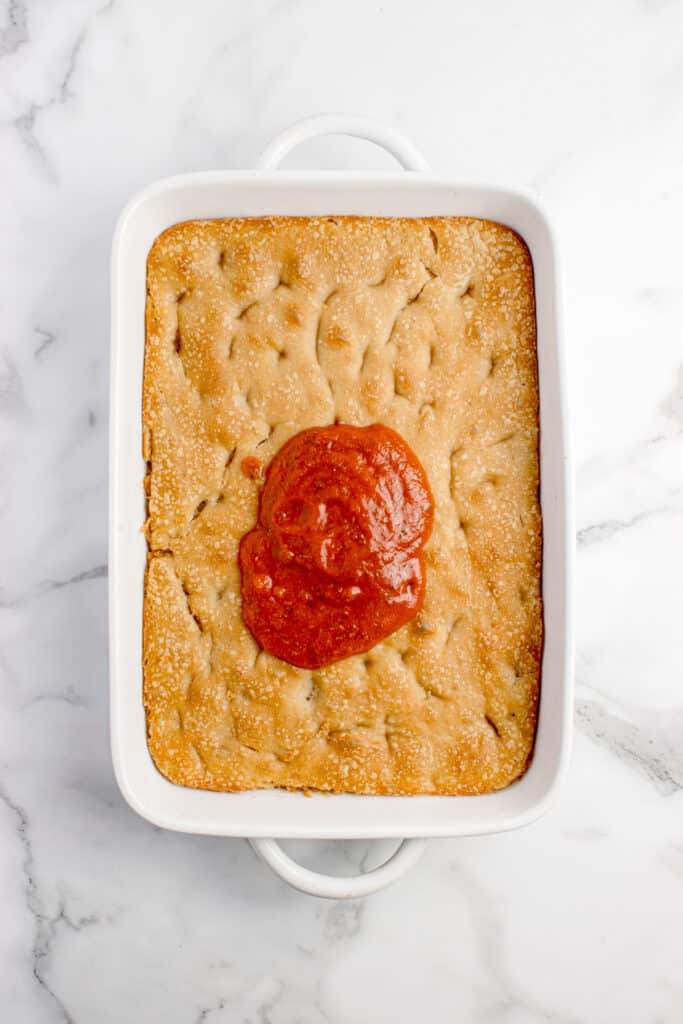 baked focaccia in white baking pan with pizza sauce in the center