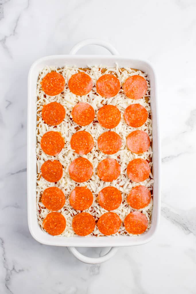 focaccia in white baking dish with cheese on top and pepperoni arranged in ordered lines